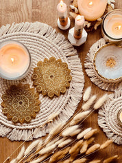 2 handgemachte Mandala Untersetzer aus goldfarbenem Resin mit filigranem Design auf dekorativem Tisch mit Kerzen und Trockenblumen