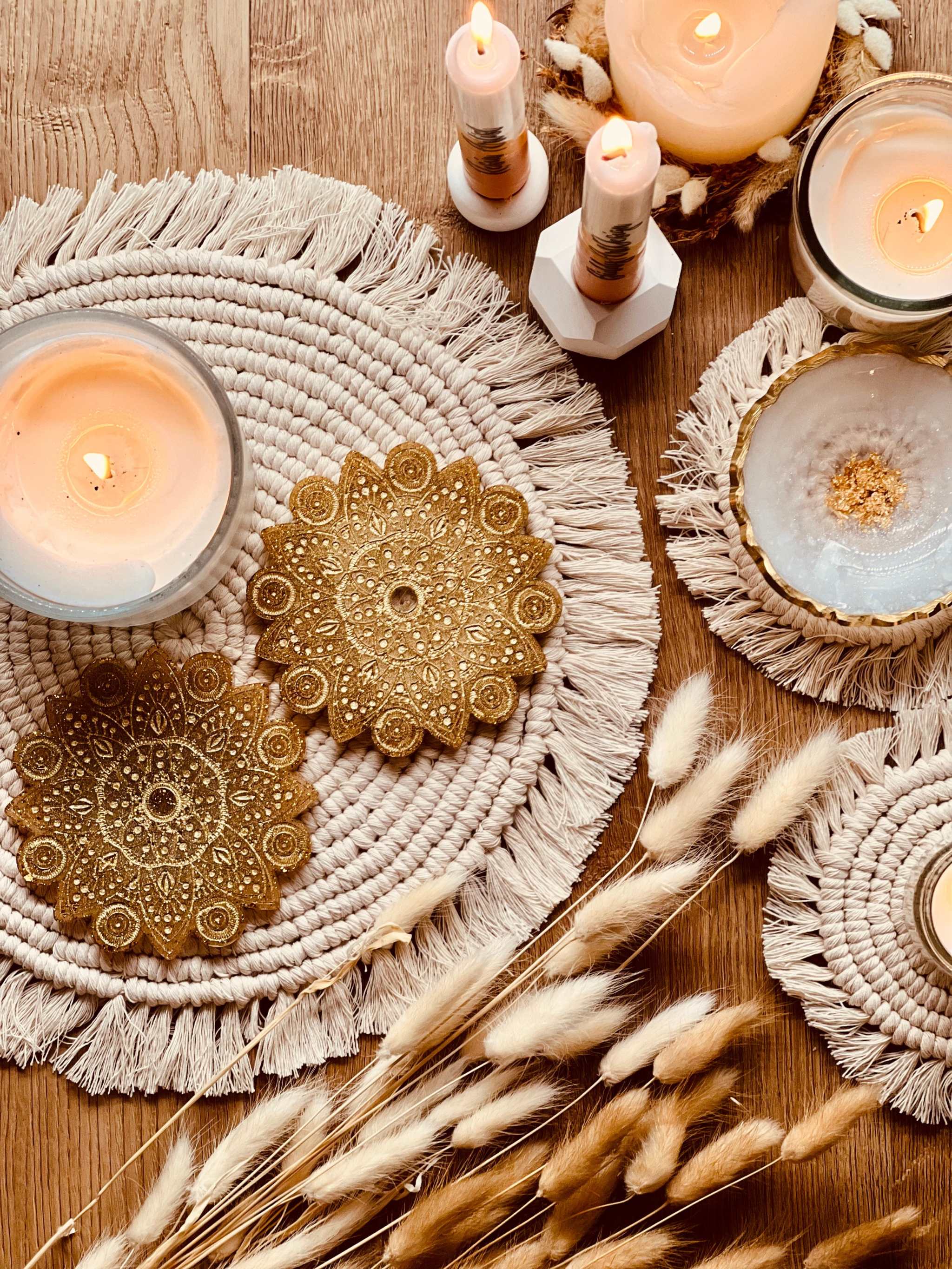 2 handgemachte Mandala Untersetzer aus goldfarbenem Resin mit filigranem Design auf dekorativem Tisch mit Kerzen und Trockenblumen