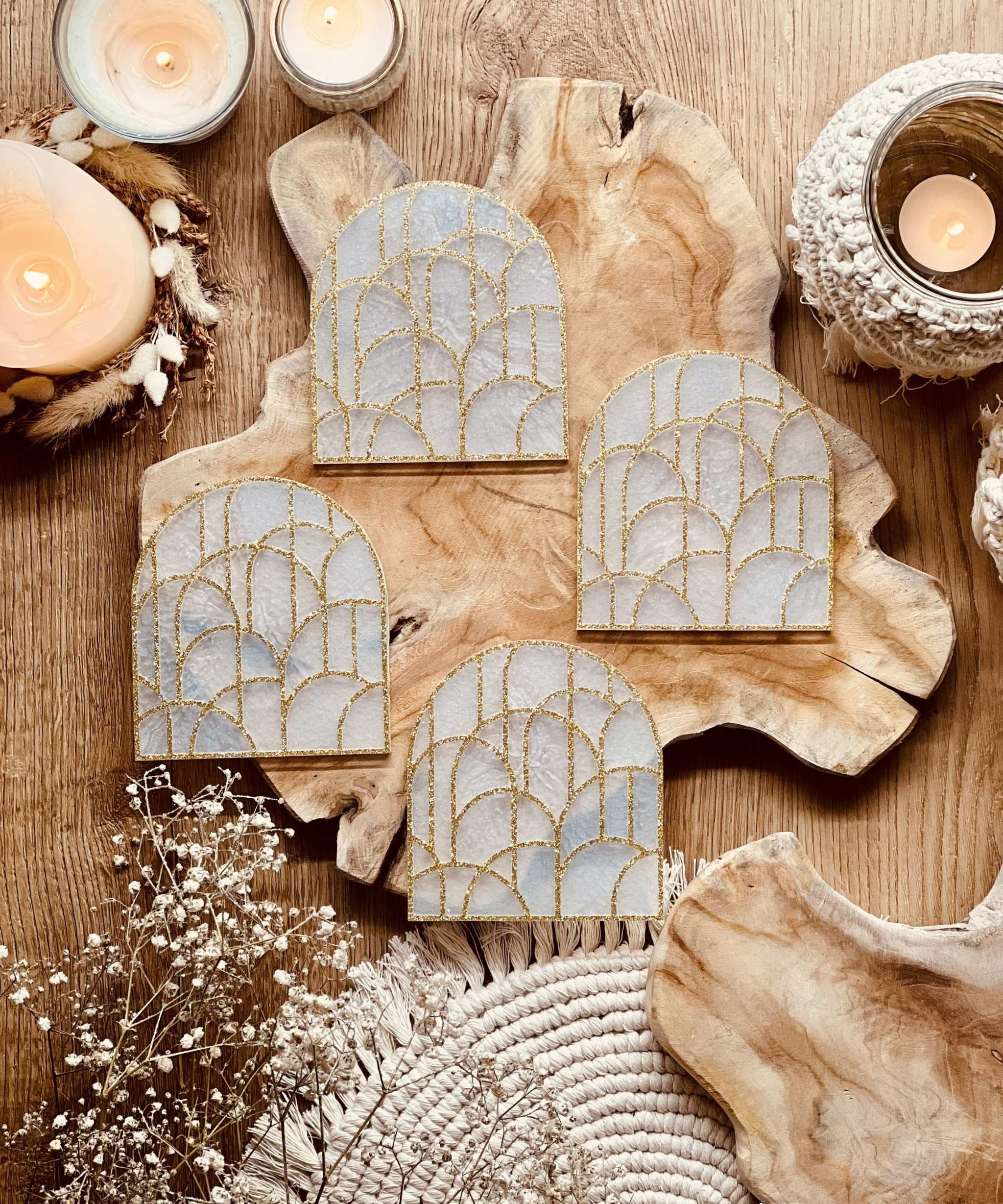 Vier geometrische Untersetzer aus weißem Resin mit goldenem 3D-Design auf Holztisch mit Kerzen dekoriert