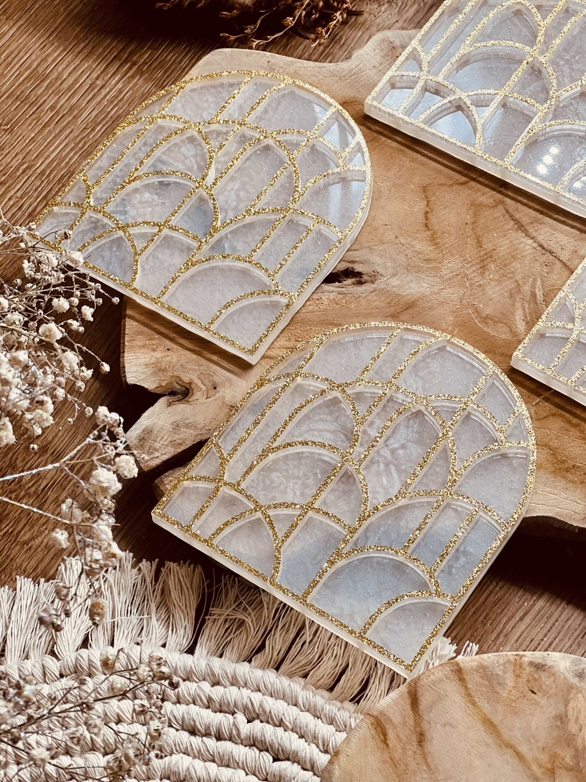vier geometrische Untersetzer aus weißem Resin mit goldenen 3D-Details auf Holztisch