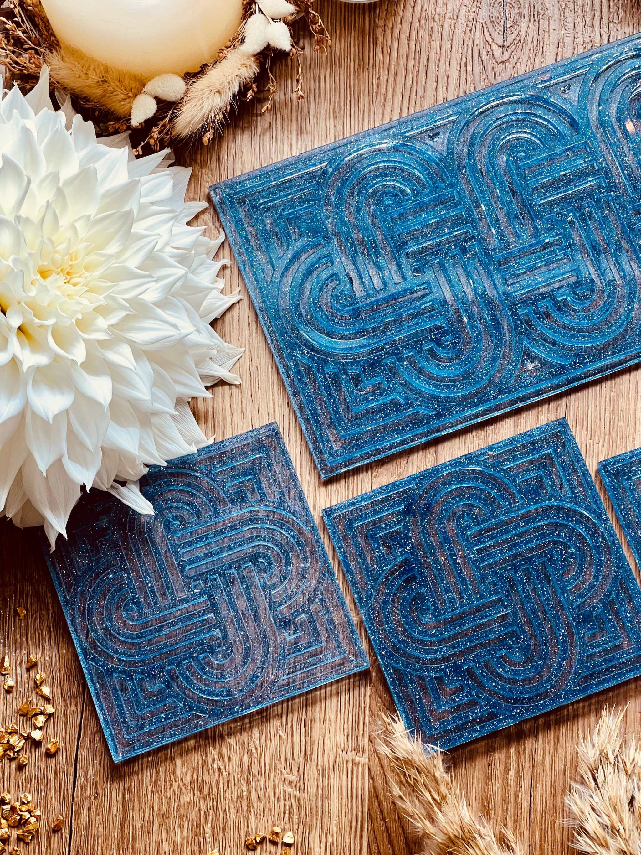 Tablett und 4 Untersetzer aus blauem Resin mit glitzerndem Knot Design auf Holzuntergrund neben weißer Blume und dekorativen Elementen
