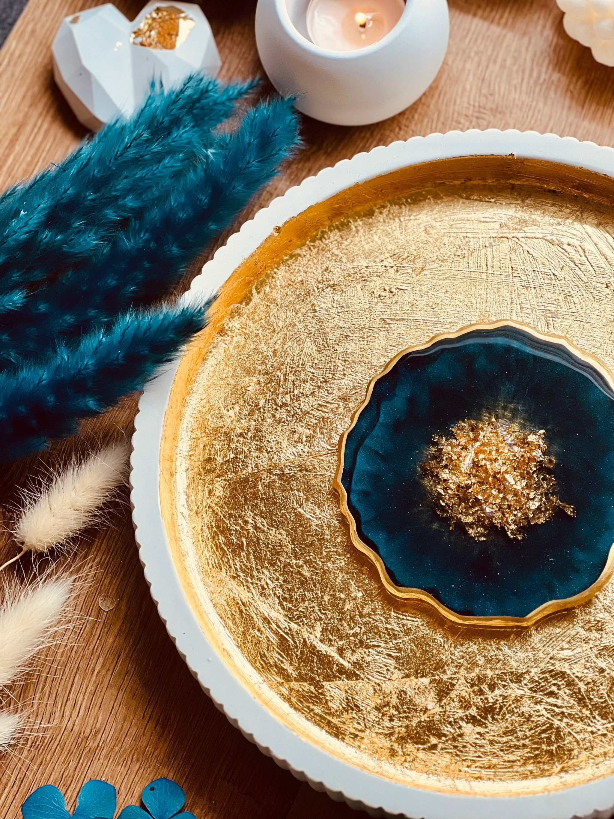 Handgemachter Untersetzer aus Resin in Petrol mit goldenen Details und 12 cm Durchmesser auf gold glänzendem Teller