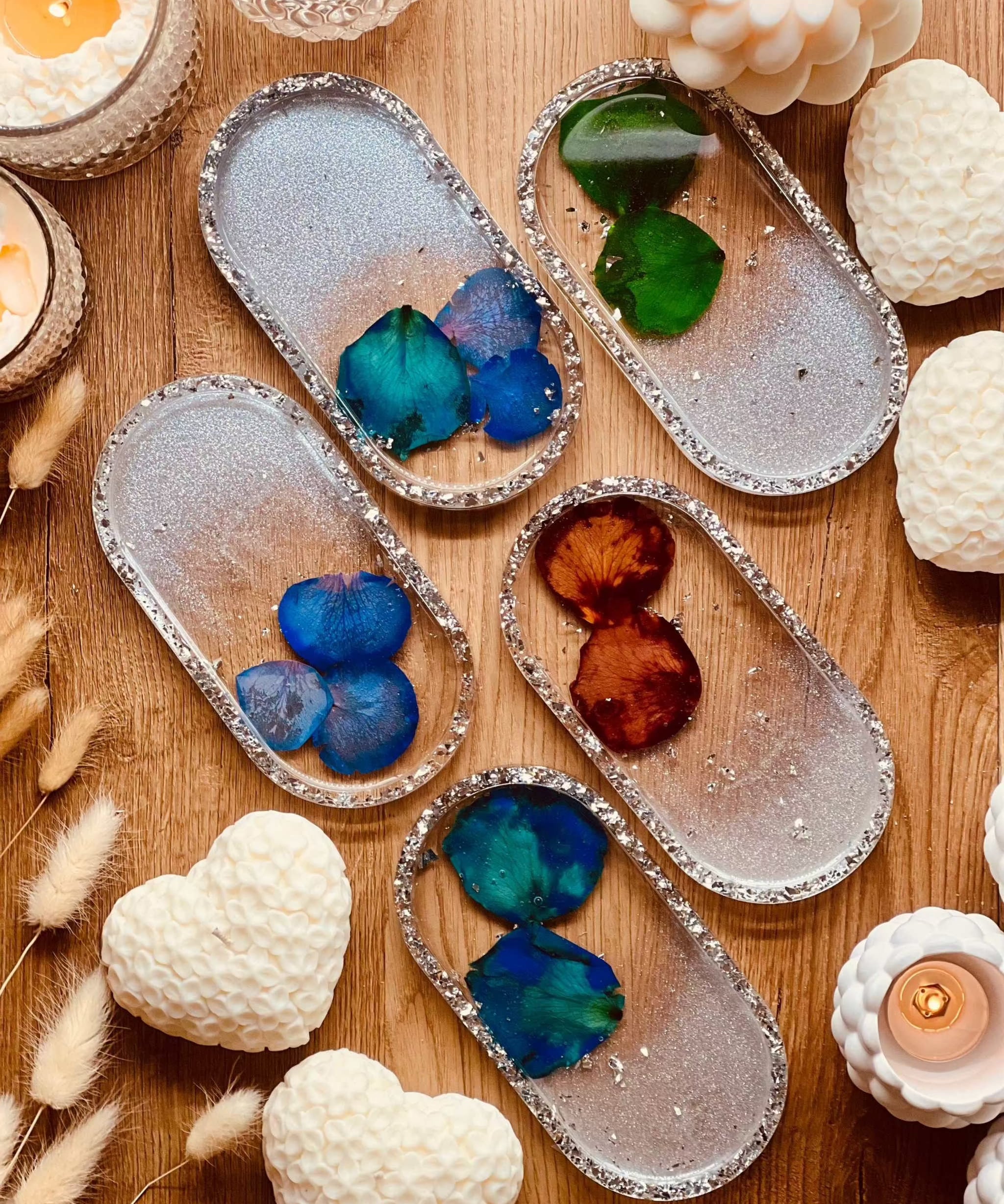 Handgemachte Schmuckschalen aus Resin mit Silberrand und farbigen Rosenblättern auf Holzuntergrund surrounded von Kerzen und Dekoration