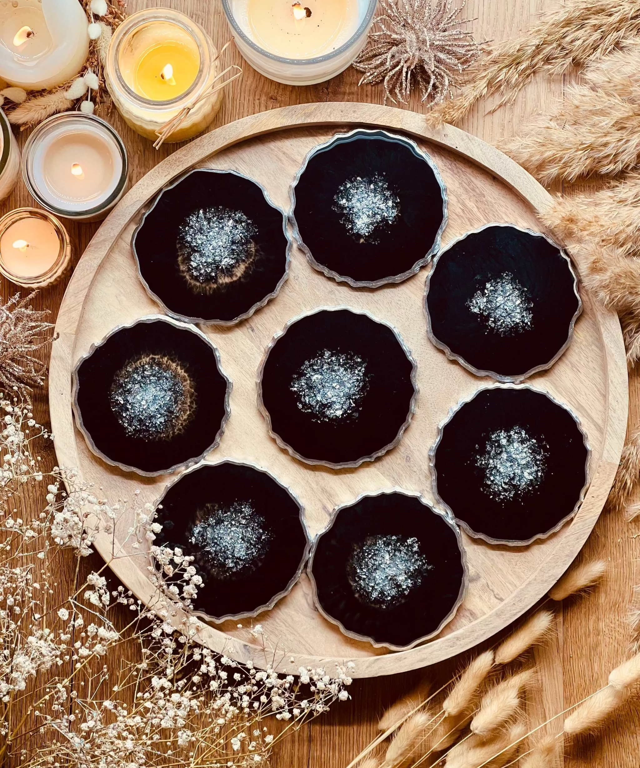 8 handgefertigte schwarze Resin Untersetzer mit silbernen Details auf rundem Holztablett