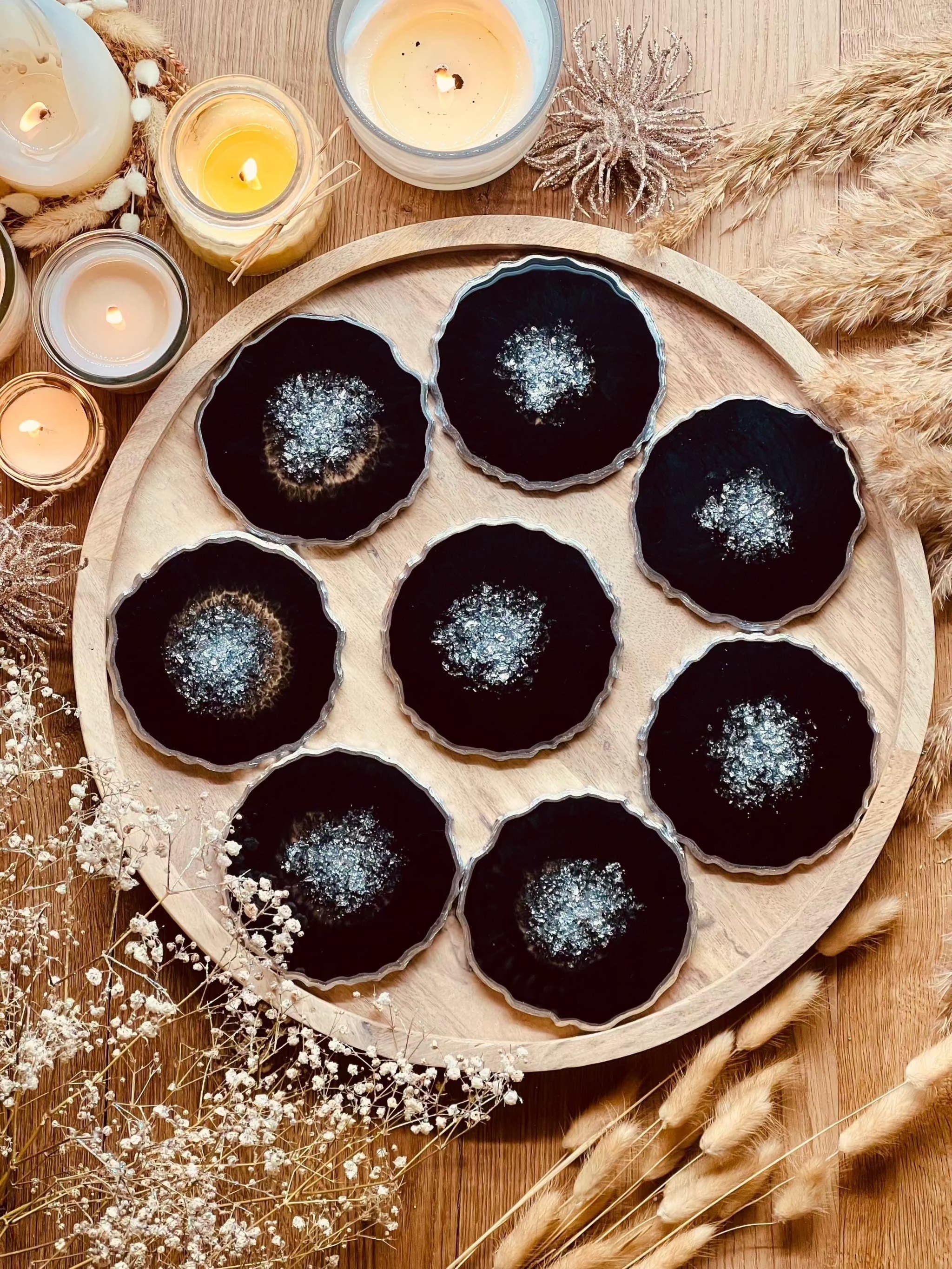 8 handgefertigte schwarze Resin Untersetzer mit silbernen Details auf rundem Holztablett
