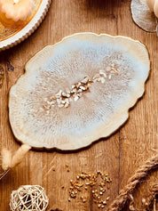 Beige handgemachtes Tablett aus Resin mit goldenen Details und Perlmuttstücken auf Holztisch