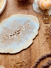 Beiges handgemachtes Tablett aus Resin mit goldenen Details und Perlmuttstücken auf Holzoberfläche