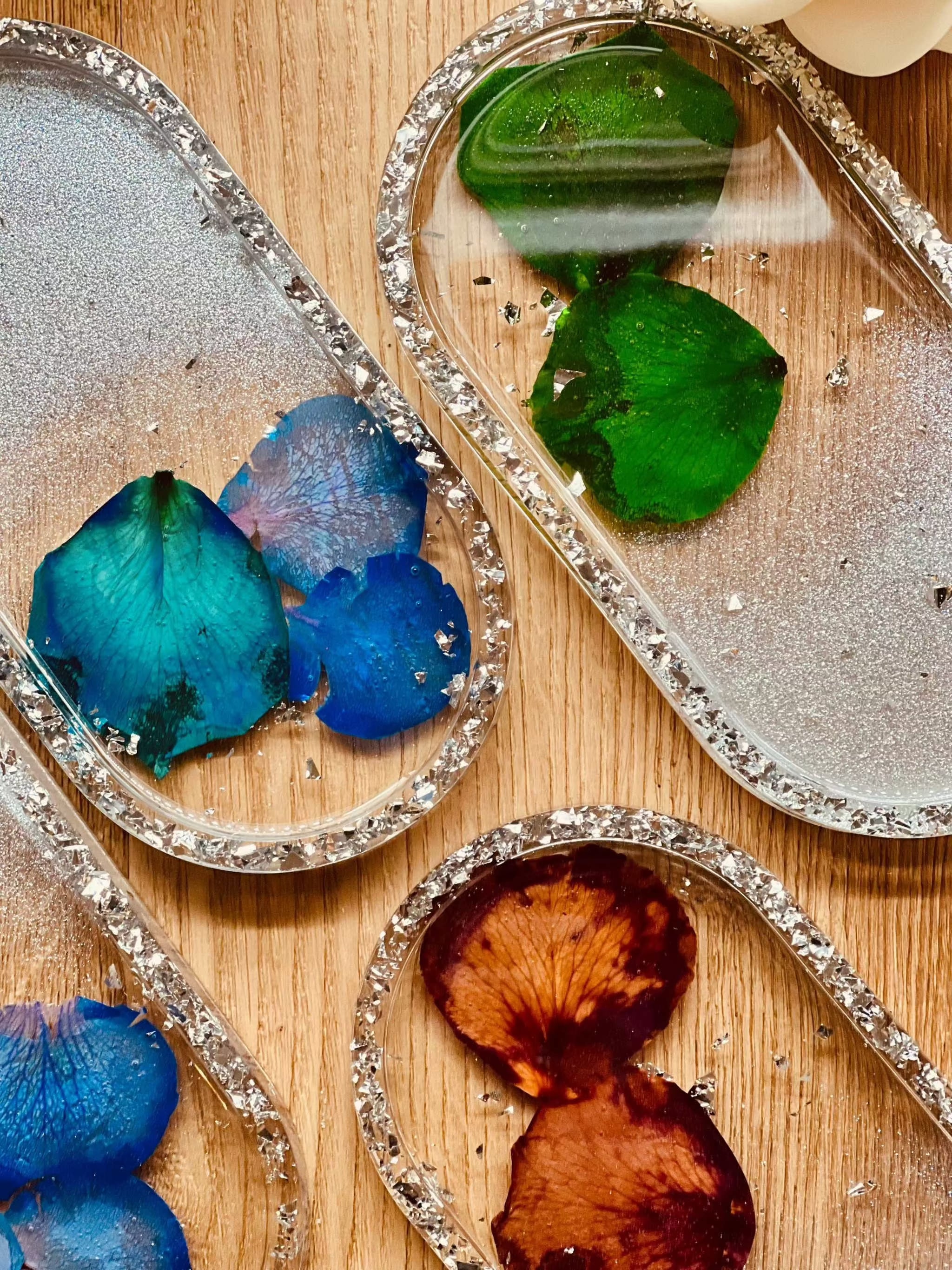 Handgemachte Schmuckschalen aus Resin mit Silberrand und farbigen Rosenblättern auf Holztisch