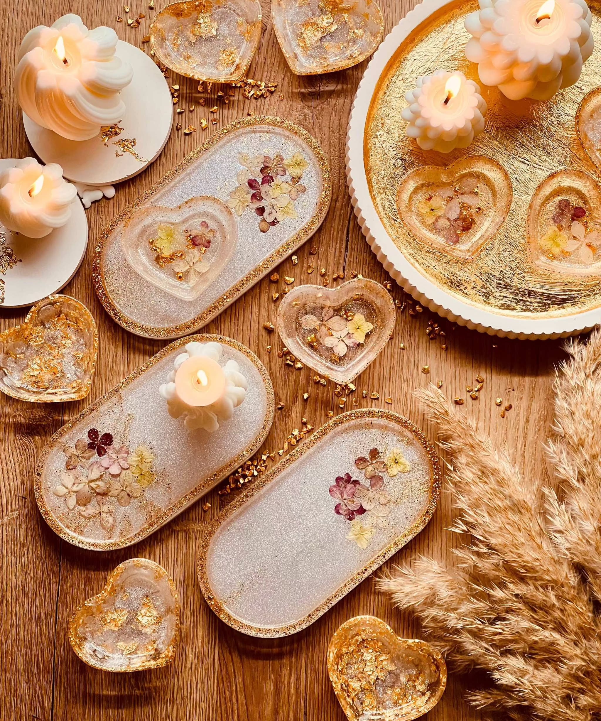 Handgefertigte weiße Schmuckschalen aus Resin mit Gold und getrockneten Blumen, dekorativ auf Holz und goldenem Tablett arrangiert.