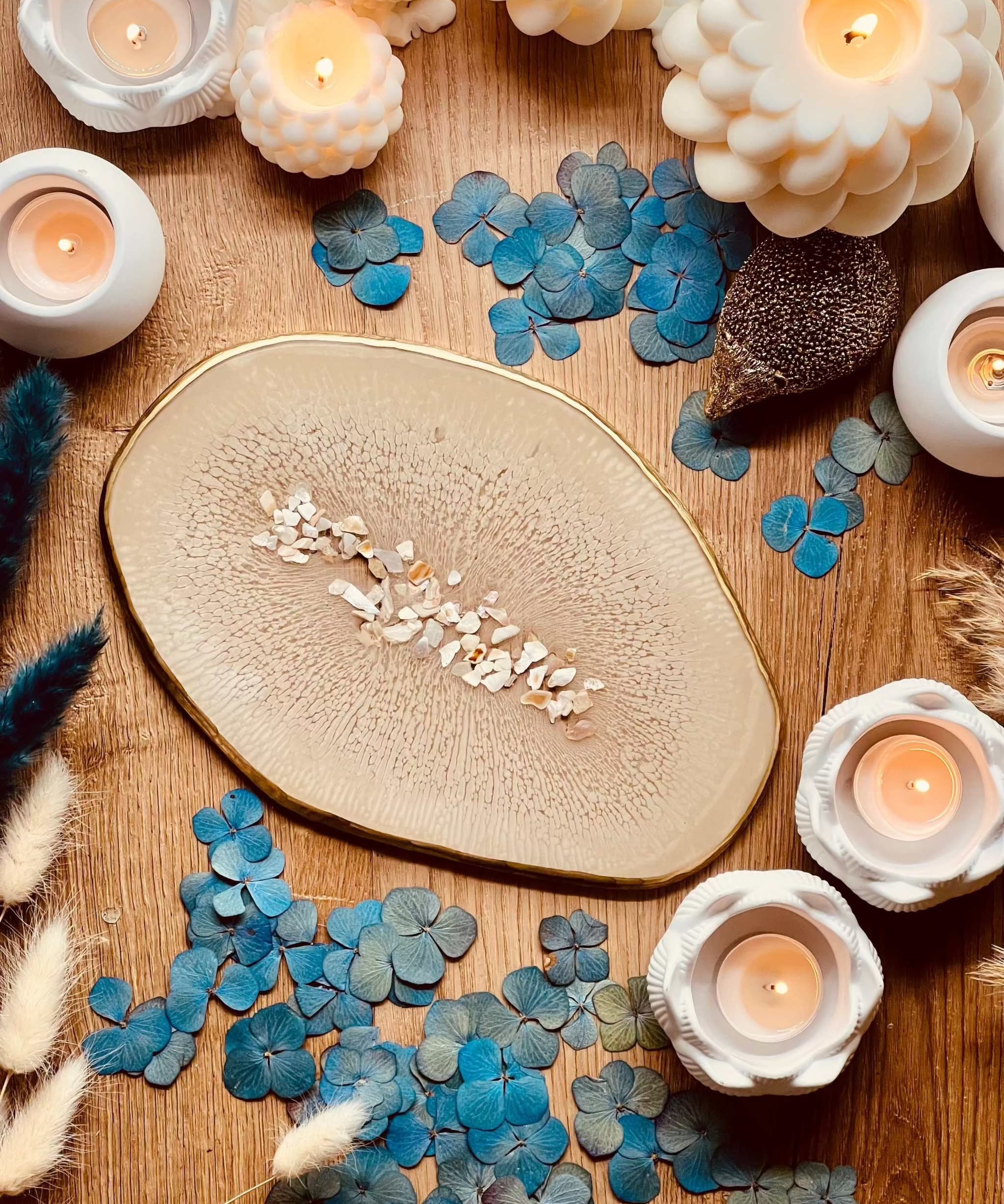 Beiges handgemachtes Tablett aus Resin mit goldenen Details und Perlmutt auf Holztisch mit Kerzen und blauen Blüten dekoriert