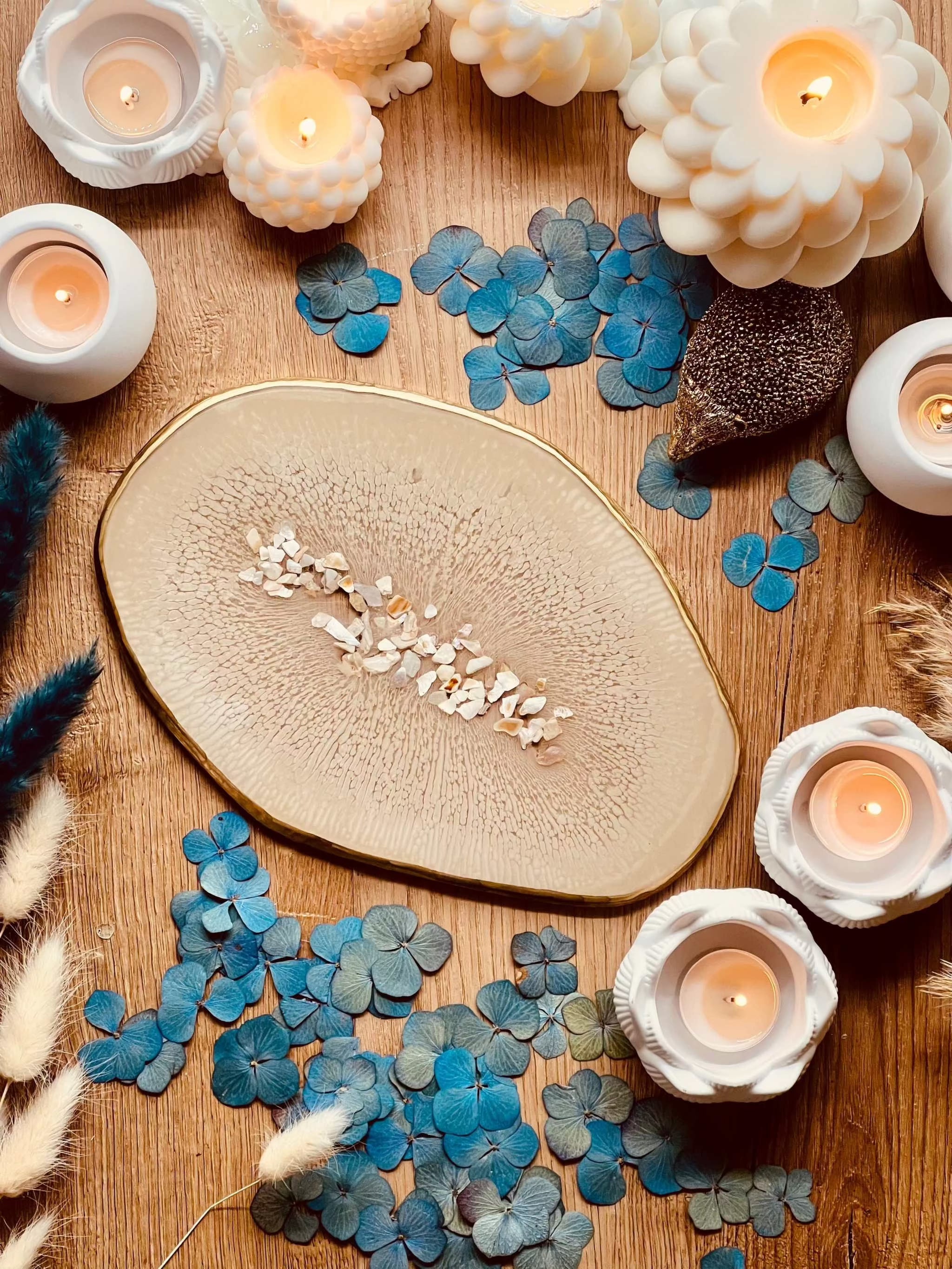 Beiges handgemachtes Tablett aus Resin mit goldenen Details und Perlmutt auf Holztisch mit Kerzen und blauen Blüten dekoriert