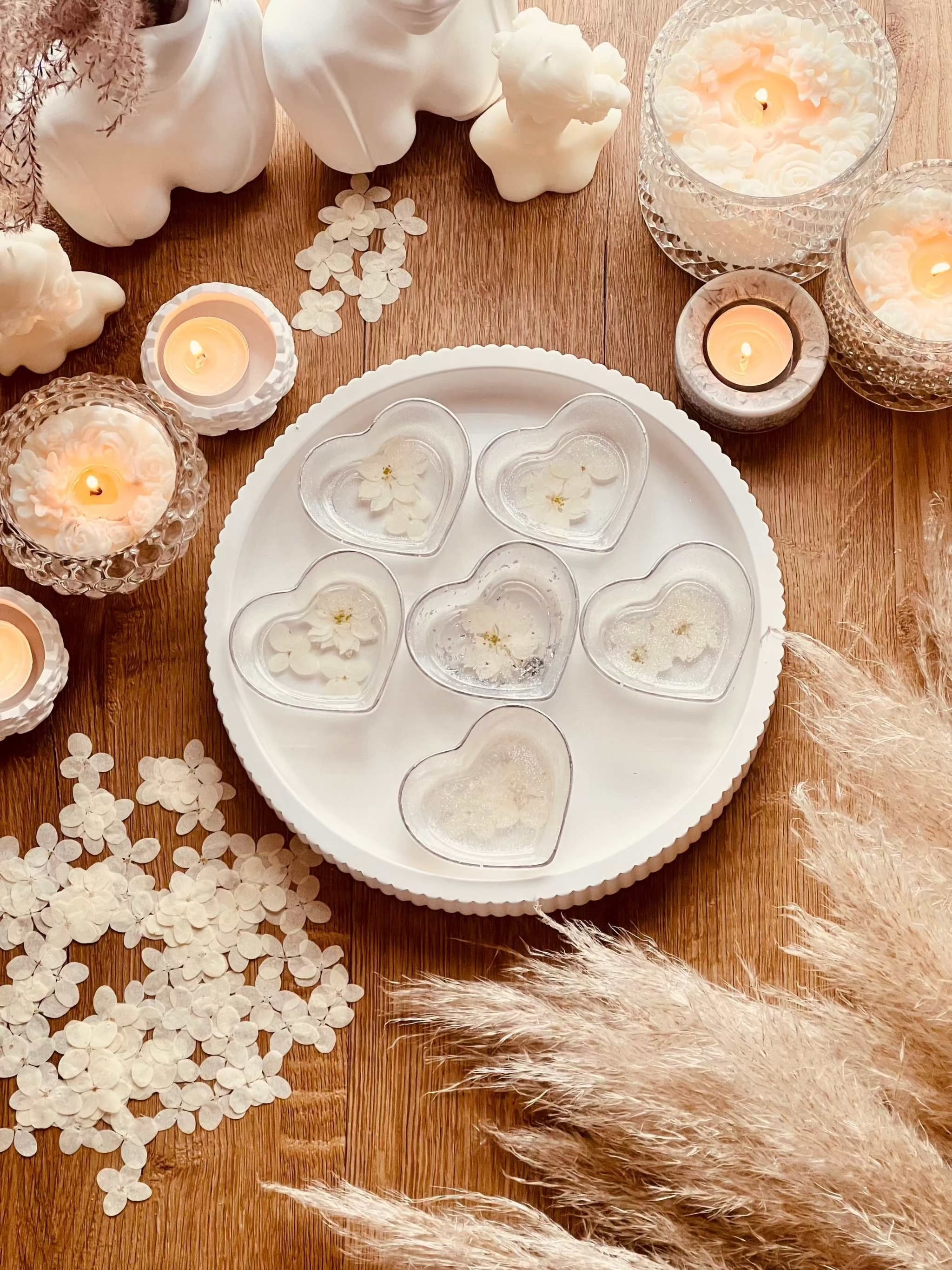 Handgemachte weiße Schmuckschalen aus Resin in Herzform mit silbernen Details und getrockneten Blumen auf einem Tablett mit Kerzen dekoriert