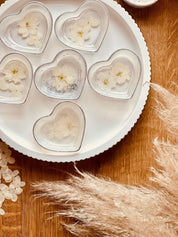 Herzförmige handgemachte Schmuckschalen aus weißem Resin mit silbernen Details und getrockneten Blumen auf weißem Teller