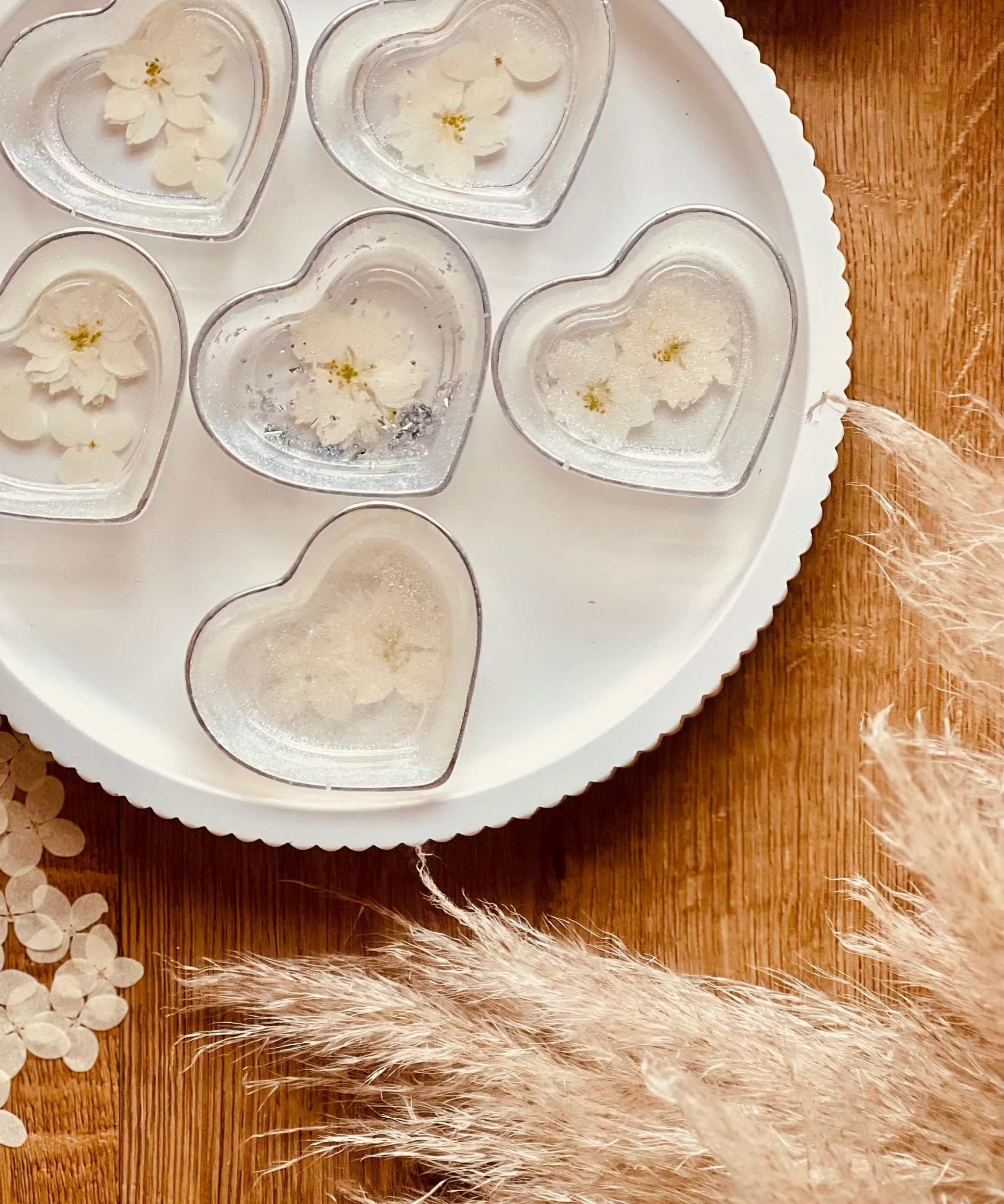 Herzförmige handgemachte Schmuckschalen aus weißem Resin mit silbernen Details und getrockneten Blumen auf weißem Teller
