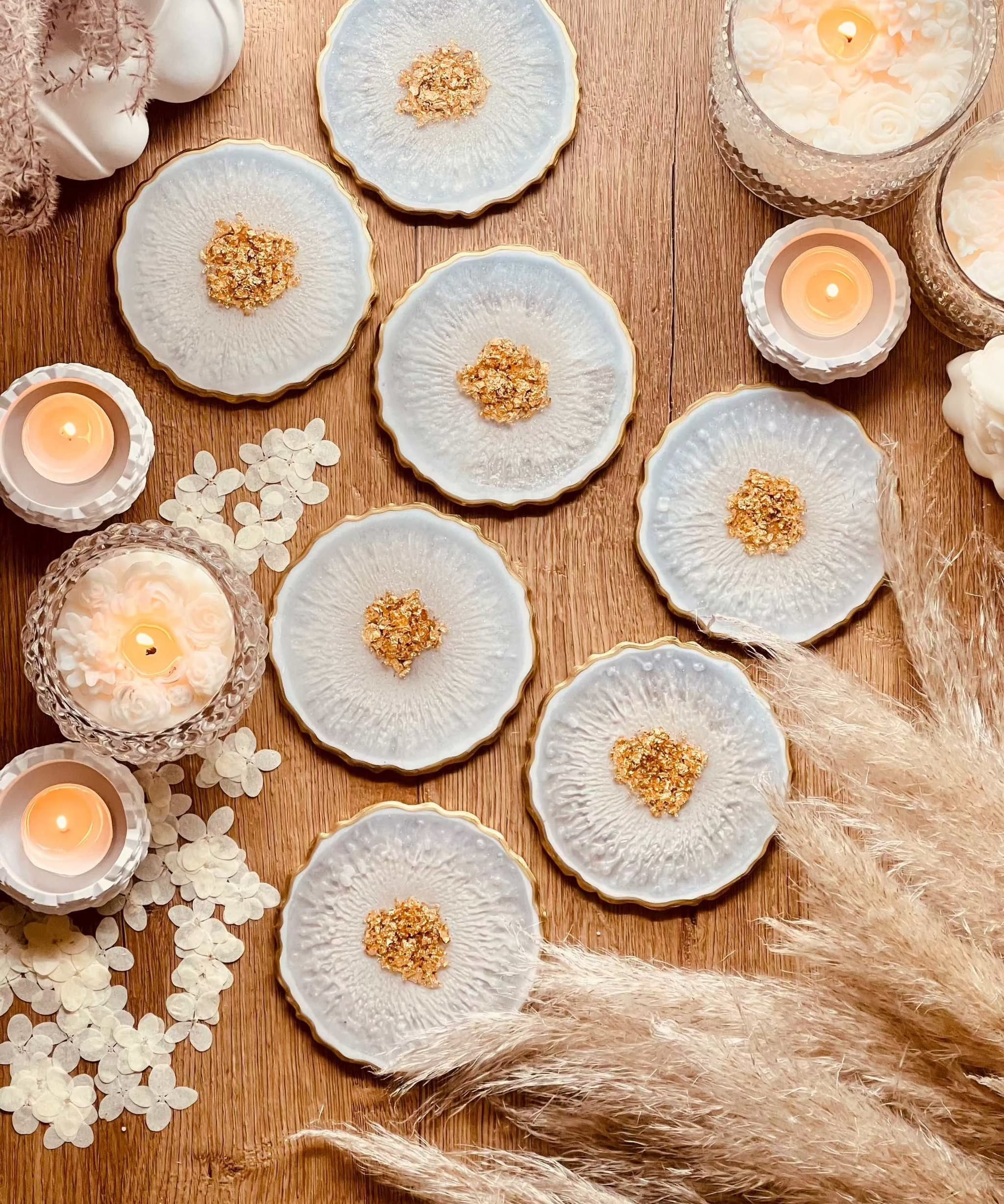 7 klassische Untersetzer aus weißem Resin mit goldenen Details, handgemacht, dekorativ auf Holztisch mit Kerzen und Trockenblumen