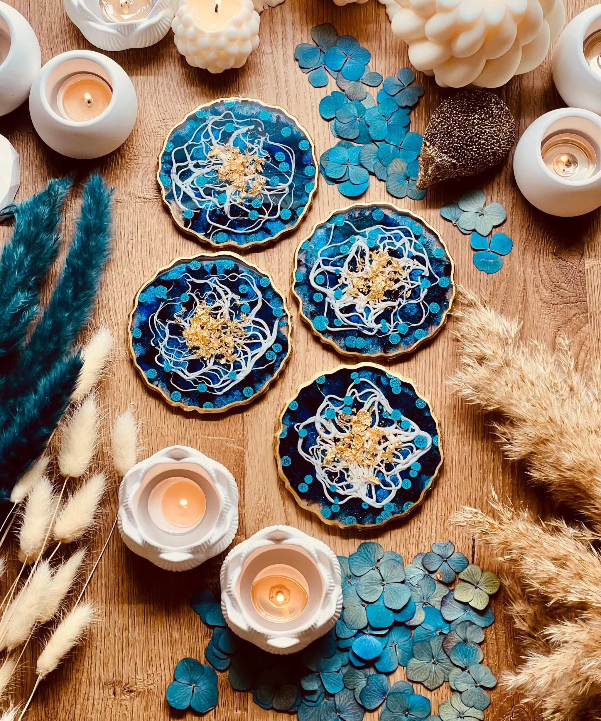 4 Untersetzer aus Resin in Blau und Weiss mit goldenen Details als handgemachtes 4-teiliges Set auf Holztisch mit Kerzen und Dekoration