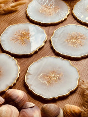 4 elegante Untersetzer aus weißem Resin mit goldenen Details und gezacktem Rand auf Holztisch